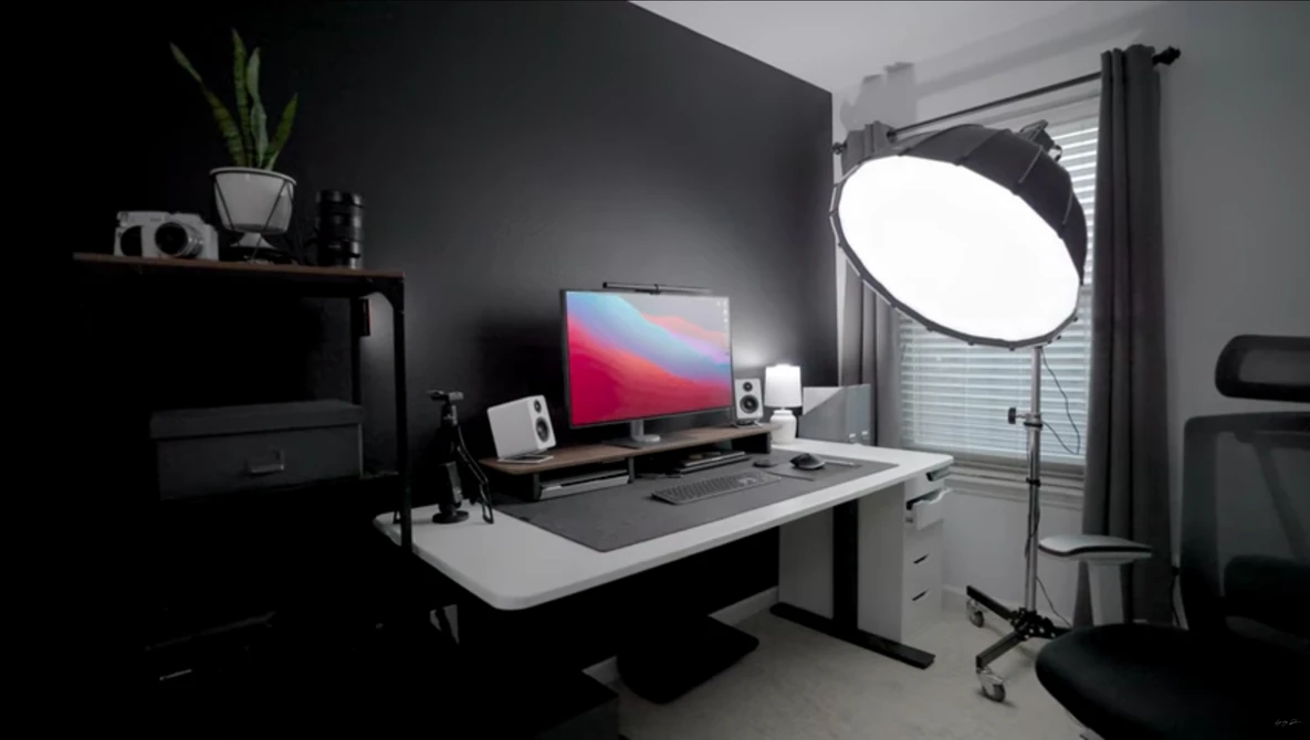 Professional photography studio setup with soft-box lighting, monitor displaying gradient wallpaper, and organized desk workspace.