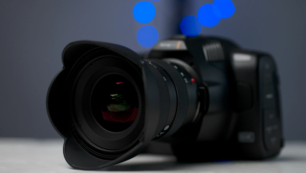 Professional mirrorless camera with wide-angle lens attached, positioned on white surface with blurred blue bokeh lights in background.