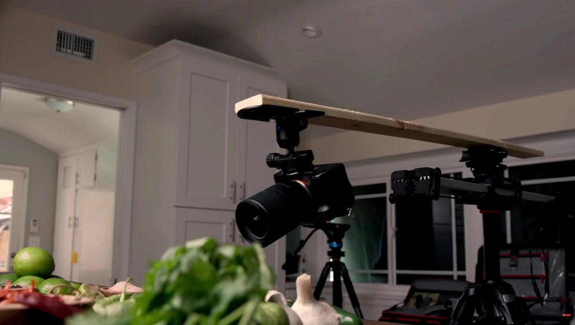 Professional camera mounted on tripod with overhead lighting rig in kitchen studio setup.