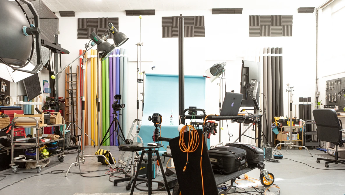 Professional photography studio with lighting rigs, colored backdrop panels, tripods, and production equipment arranged throughout an industrial space.