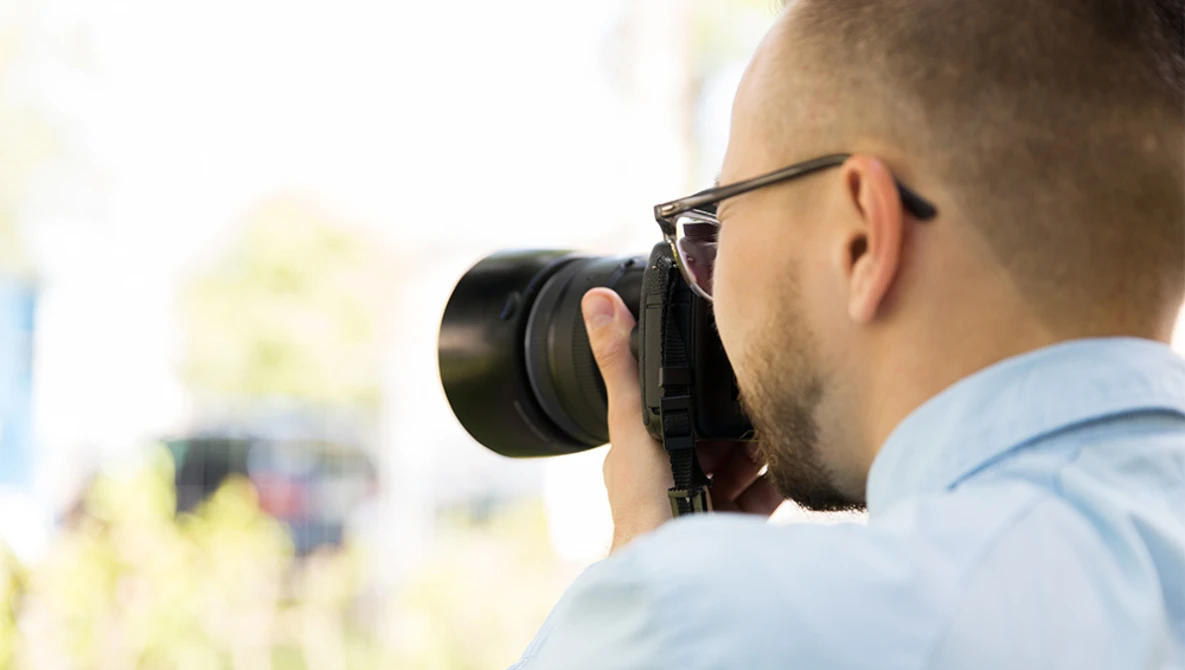 Photographer wearing glasses looking through camera viewfinder while shooting outdoors.