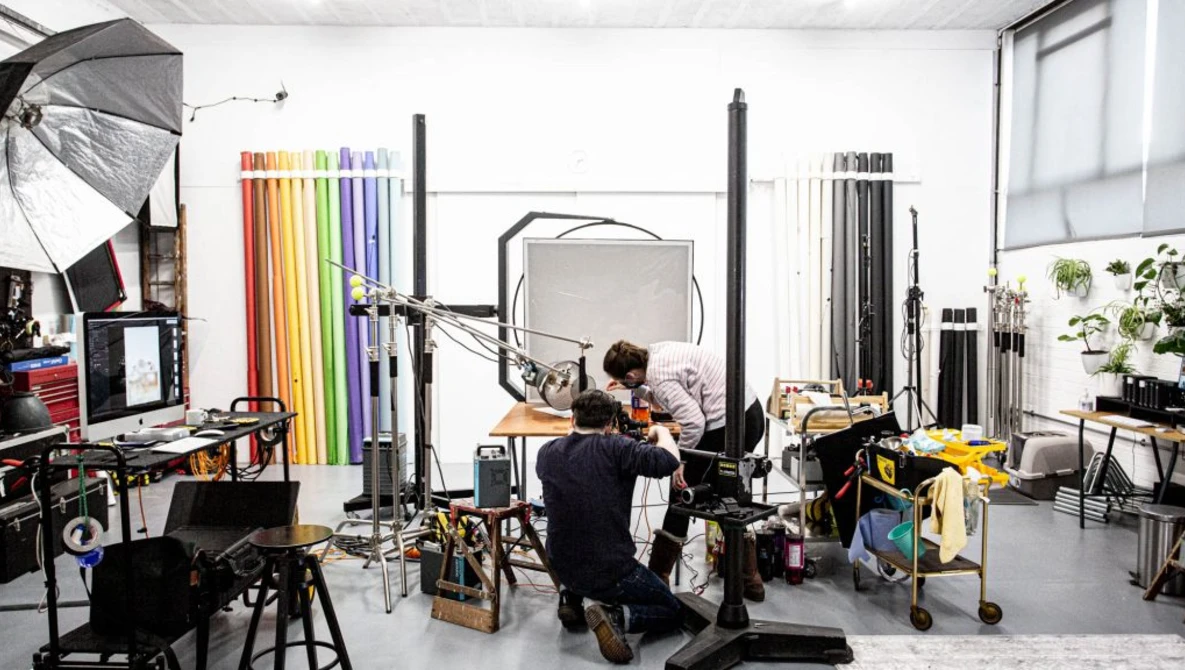 Photographer working in a studio with lighting equipment, reflectors, and color swatches on the walls.