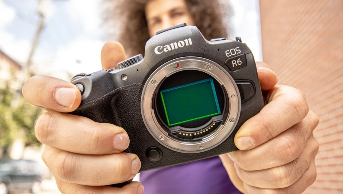 Canon EOS R6 mirrorless camera held up to display the sensor with green-tinted protective cover visible.