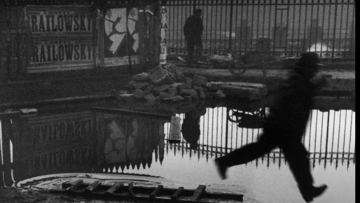 Silhouetted figure leaping over water in an urban industrial setting, captured mid-motion.