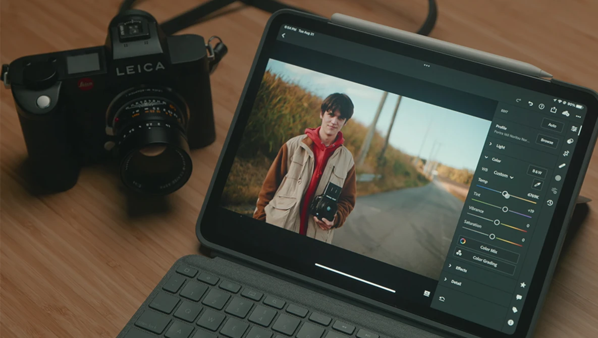 Leica M-series film camera next to tablet displaying portrait editing software with image of person in red jacket.