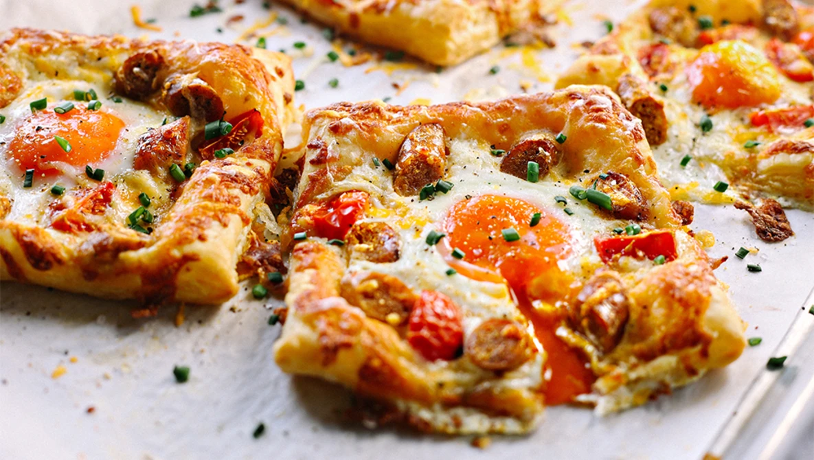 Golden-brown pizza pieces with melted cheese, red peppers, and fresh herbs scattered on white surface.