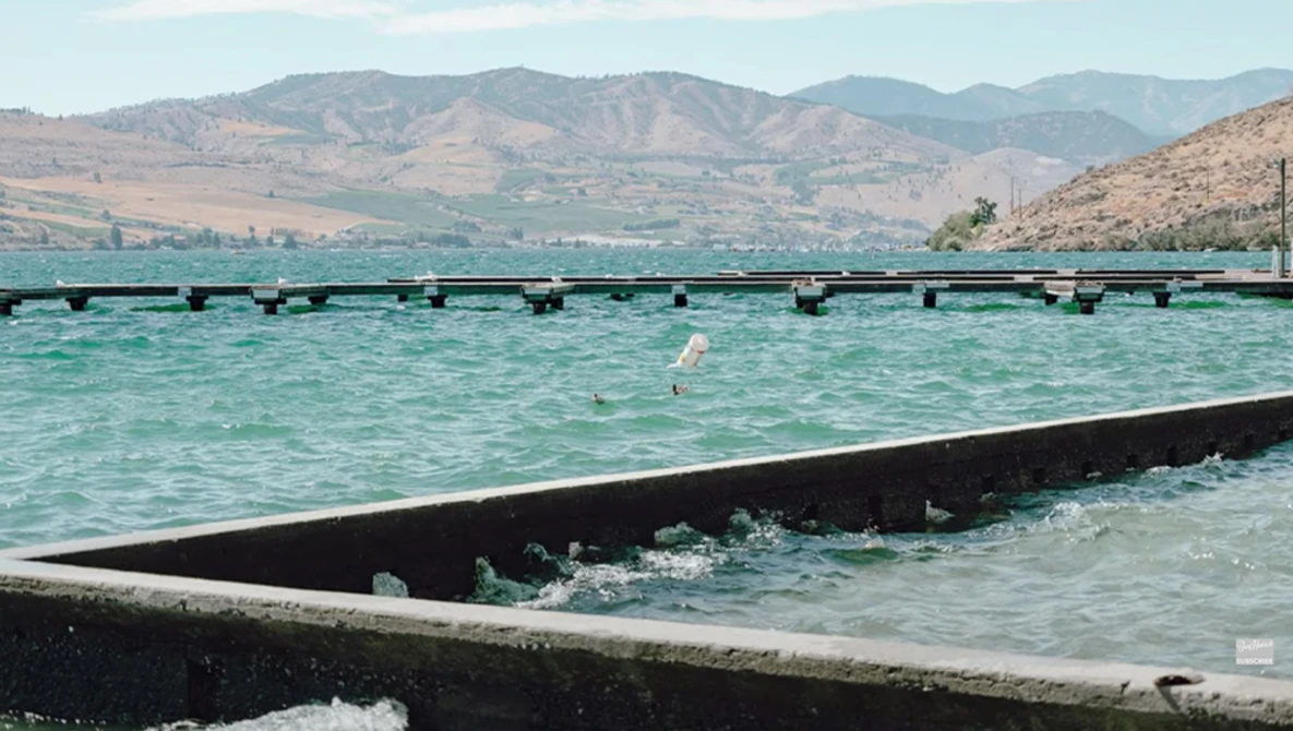 Turquoise water enclosed by black fish farm nets with arid mountains visible across the bay.