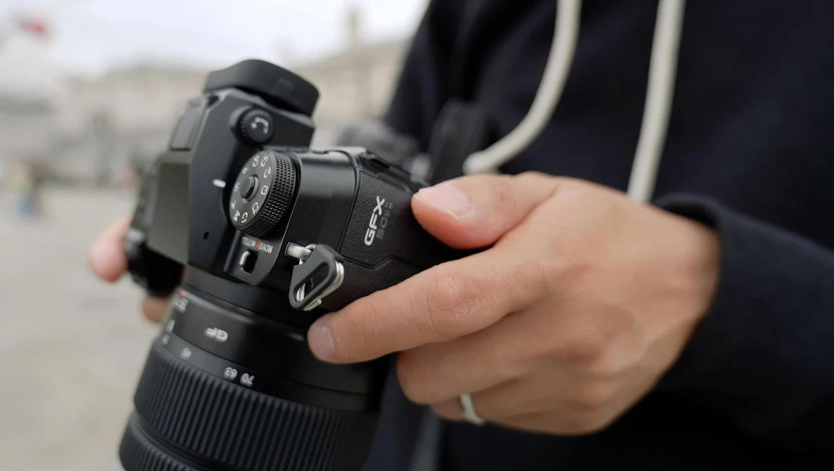 Photographer holding a DSLR camera with telephoto lens attached, wearing a black jacket with striped trim.