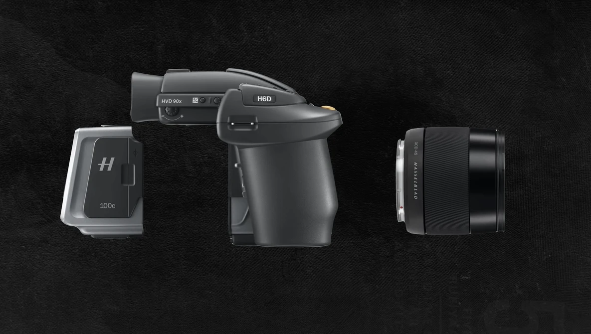 Three professional camera components arranged against a dark background: a medium format camera body with viewfinder, a battery or power module, and an interchangeable lens.