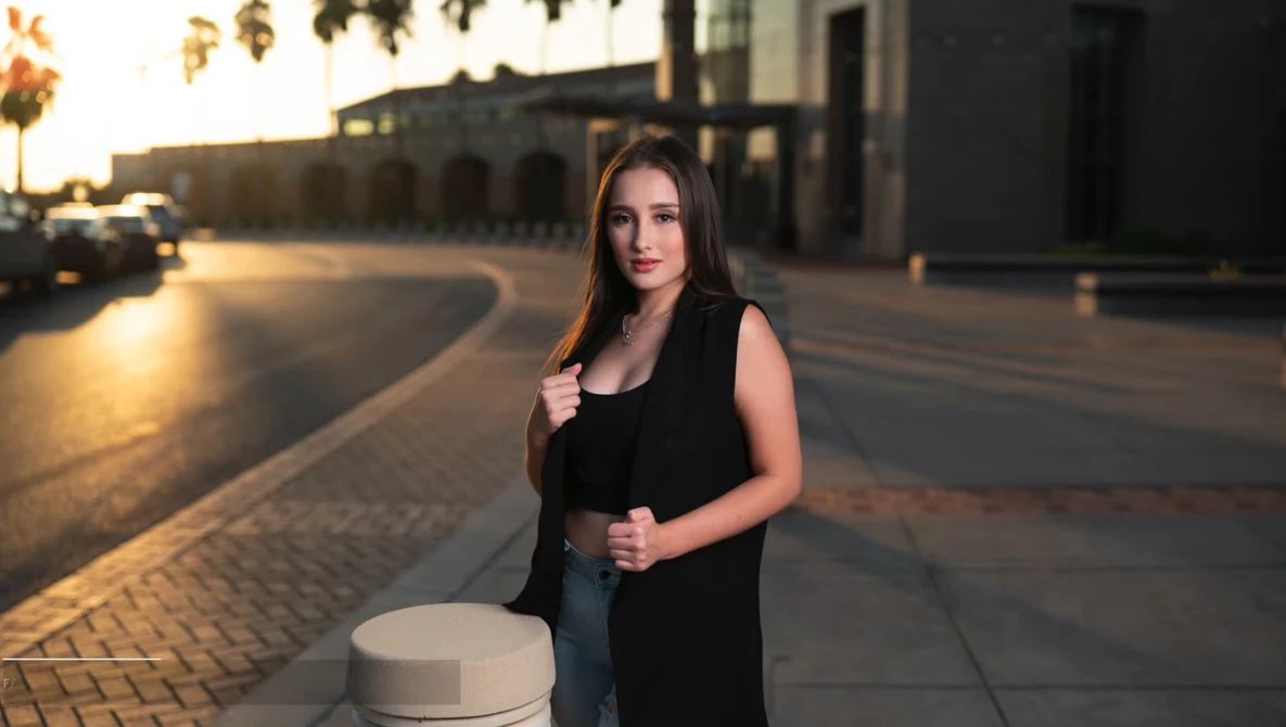 Woman in black sleeveless vest standing on a paved plaza during golden hour lighting.