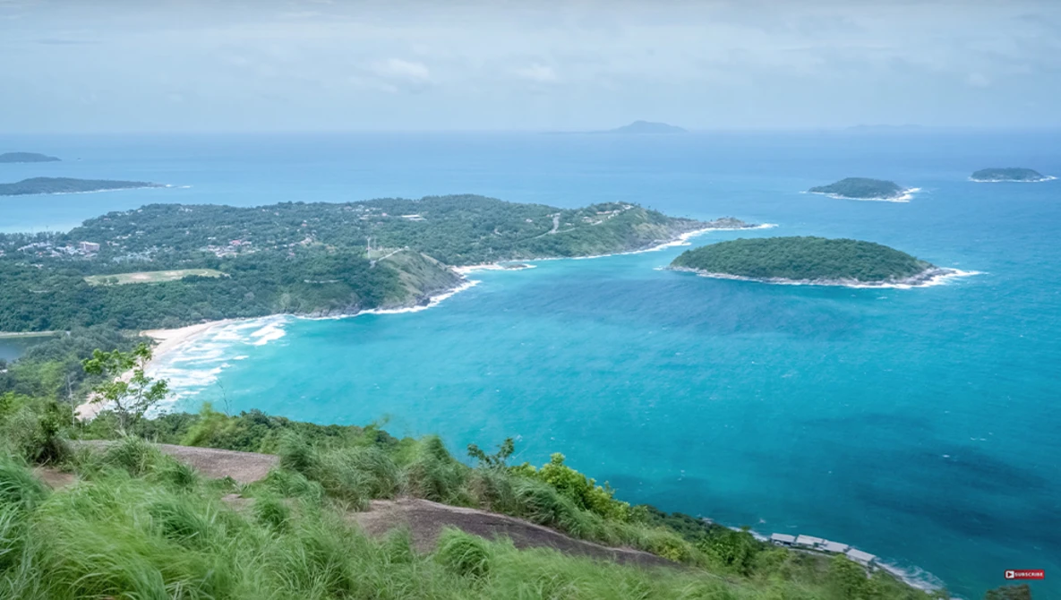 Aerial view of a tropical bay with turquoise water, white sand beach, and forested hillsides.