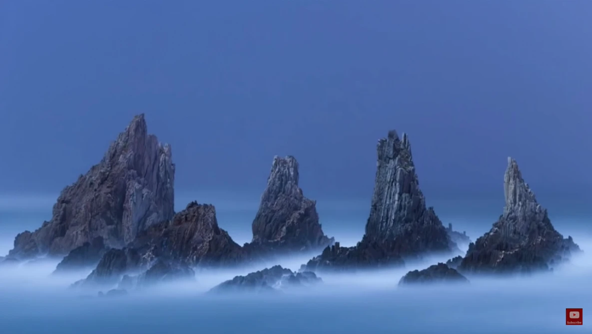 Jagged rock formations rising through heavy mist against a clear blue sky.