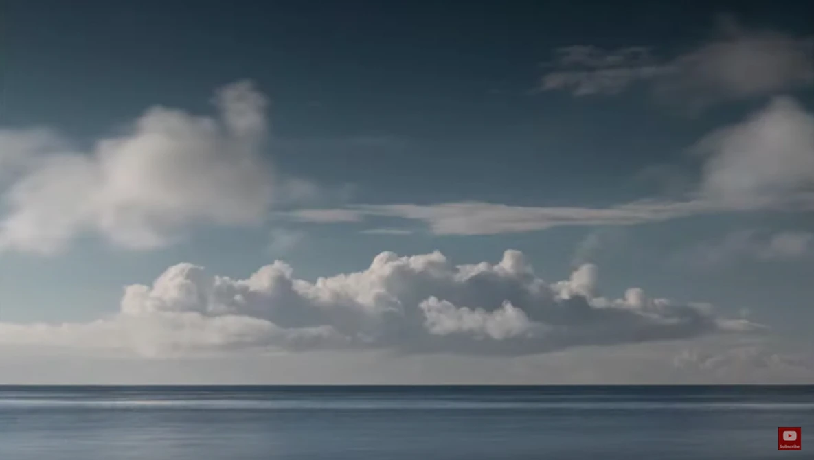 Calm seascape with puffy white clouds and blue sky above a still ocean horizon.