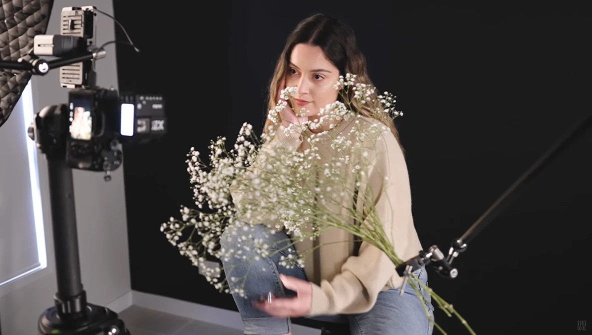 Woman holding baby's breath flowers in studio with professional lighting setup visible.