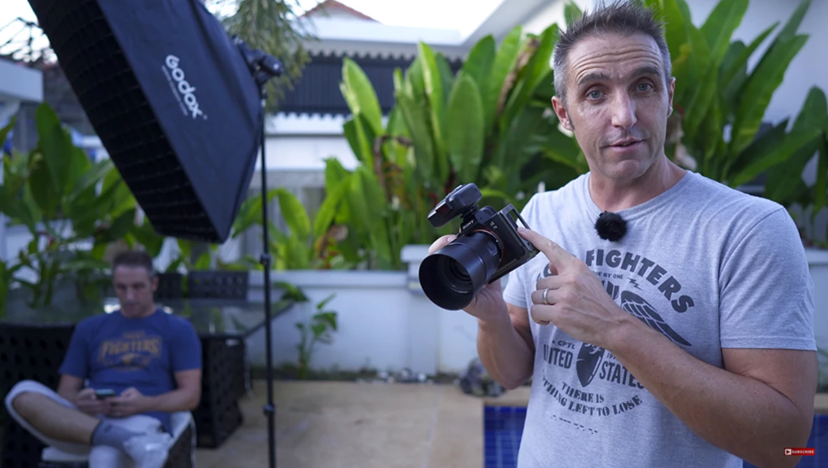 Videographer holding a professional camera during an outdoor shoot in a courtyard setting with studio lighting.