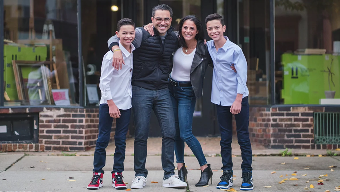 Five young people smiling at the camera while standing together on a brick-lined urban street.