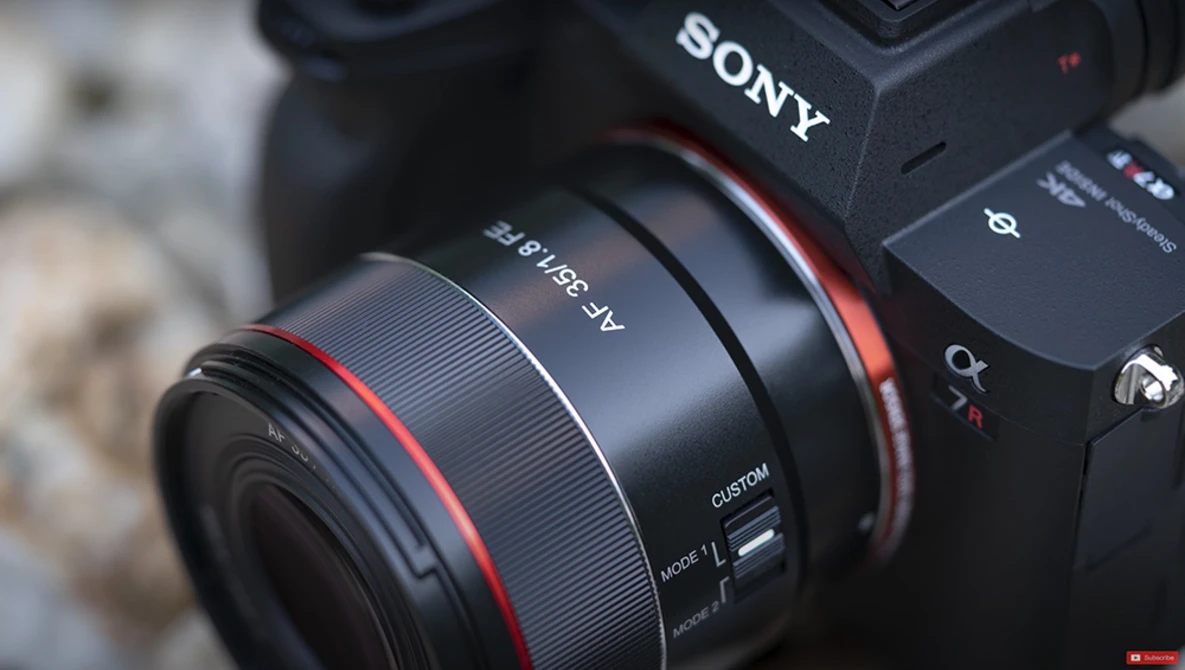 Sony mirrorless camera with red-accented lens mounted, showing camera body and lens detail in close-up.