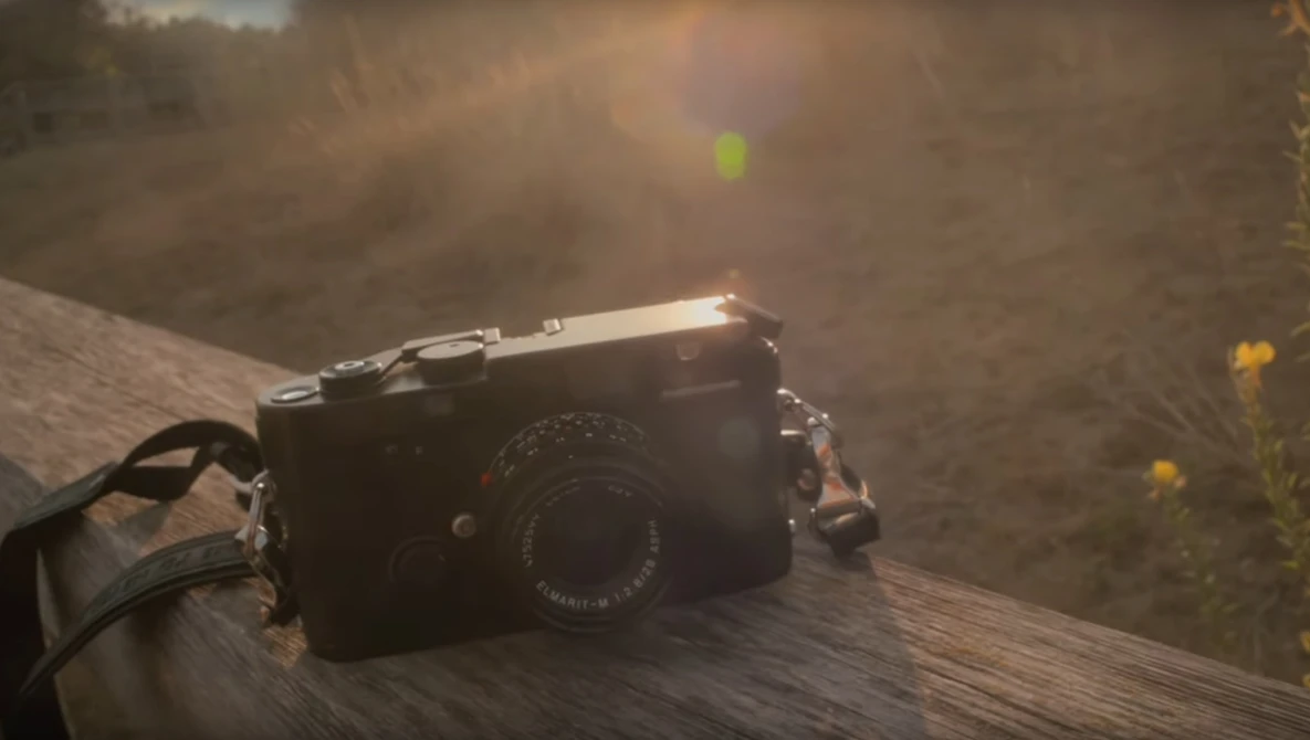 Rangefinder camera with leather strap resting on weathered wood surface in natural outdoor setting.