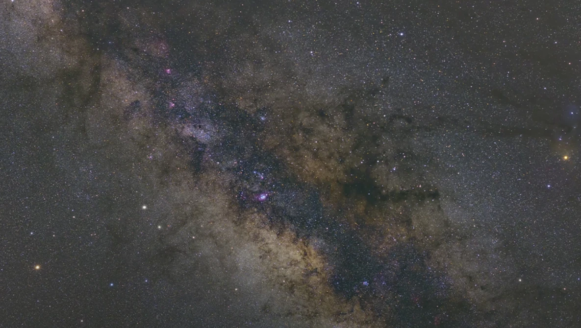 The Milky Way galaxy stretches across the night sky with vibrant purple and blue nebula regions amid dense star fields and dark dust lanes.