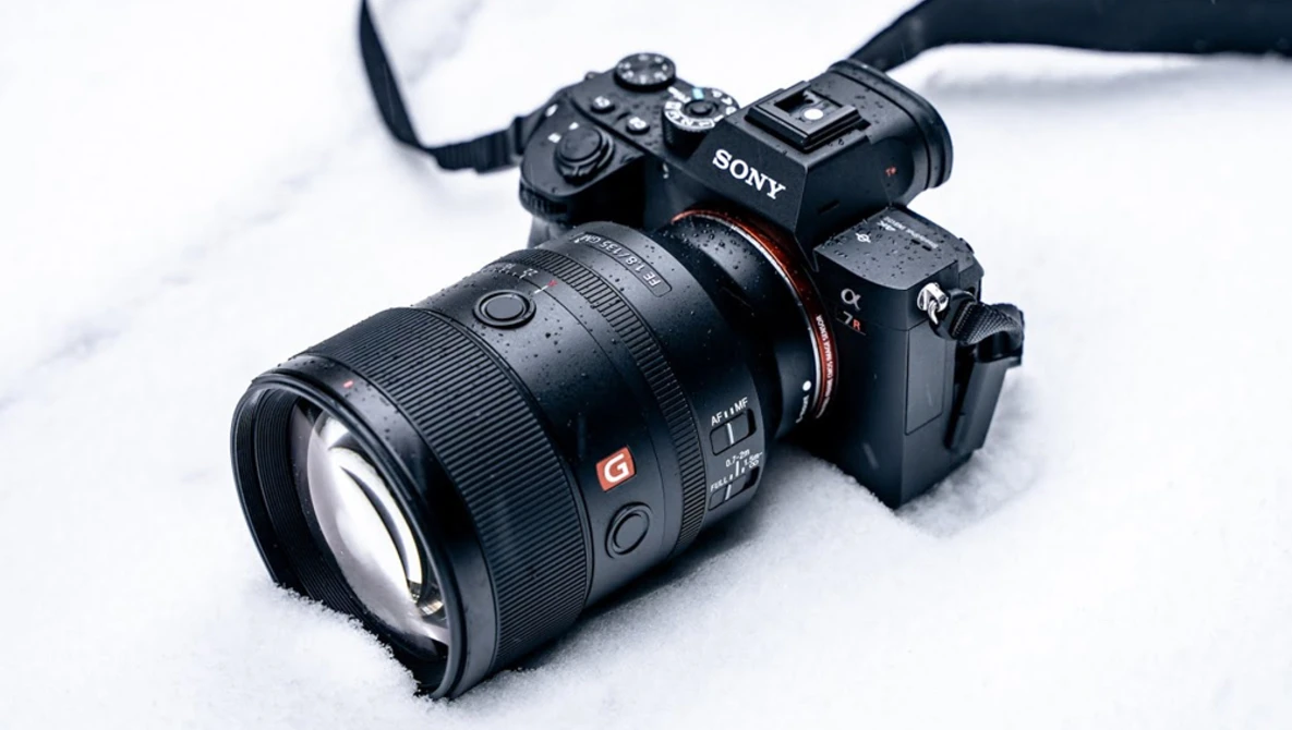 Sony mirrorless camera with telephoto lens mounted, positioned on white snowy surface.