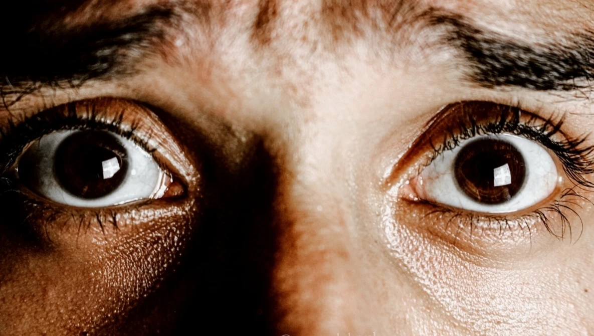 Close-up of wide-eyed human eyes with brown irises against dark background, showing intense expression.