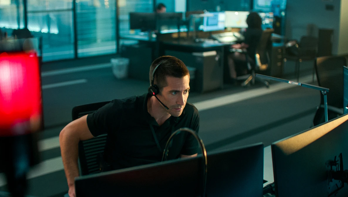 Male content creator wearing headphones while working at a computer setup in a modern office environment with red accent lighting.