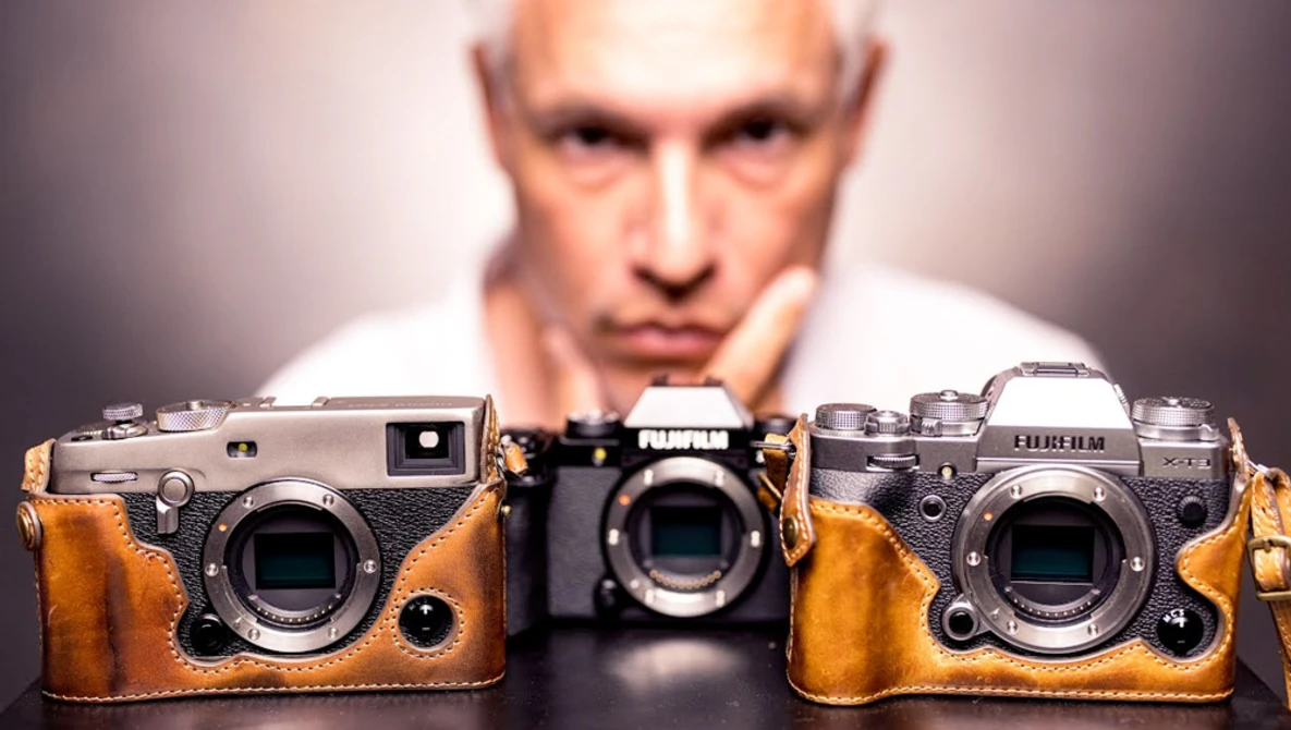 Three rangefinder cameras with brown leather cases displayed in front of a blurred male figure.