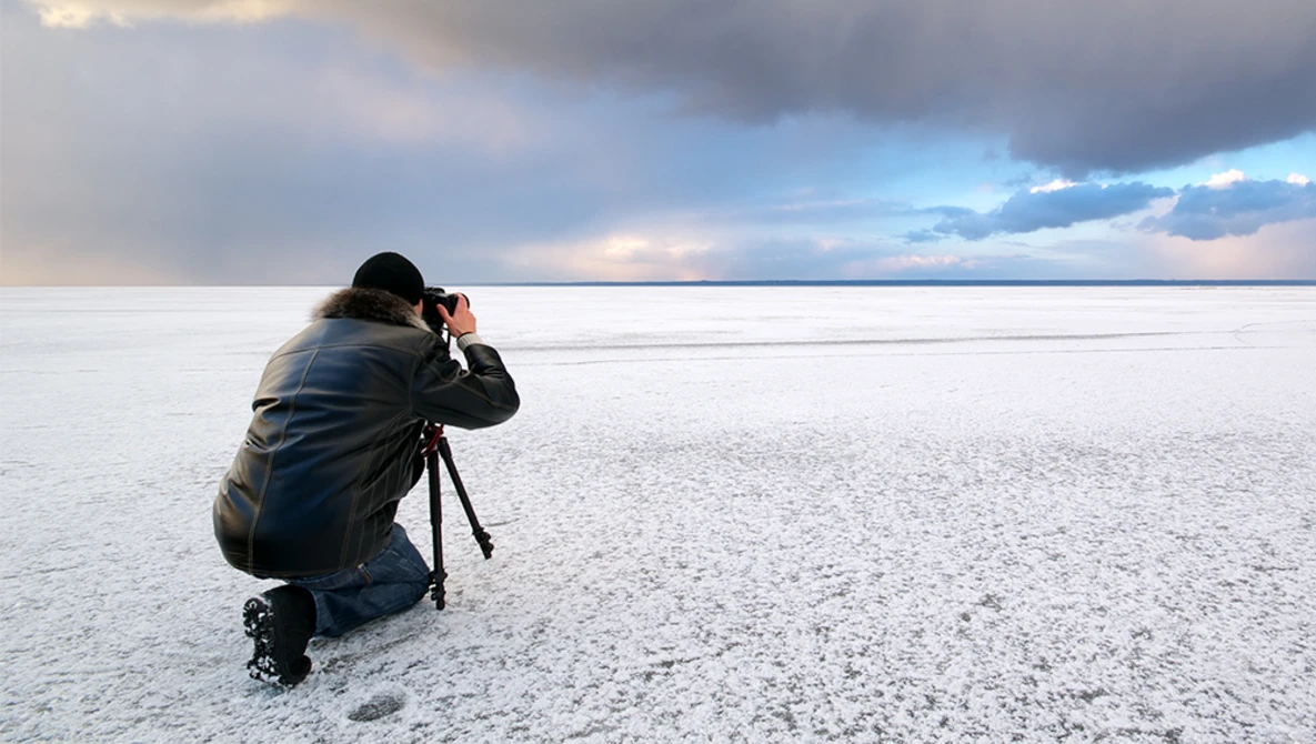 Photographer crouching on a salt flat, composing a shot with a tripod-mounted camera during golden hour.