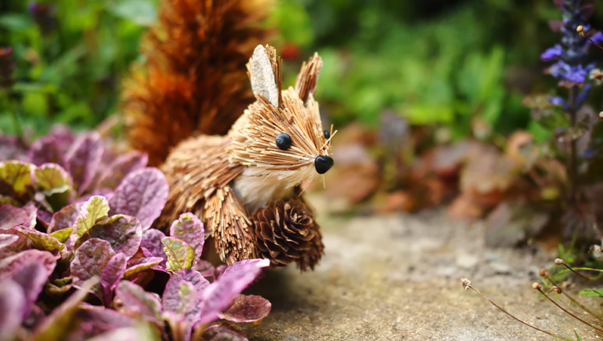 Decorative woodland creature figurine nestled among purple flowering plants and garden foliage.