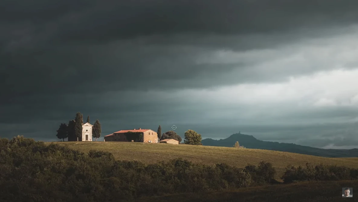 Rural chapel and farmhouse on a hillside under dramatic storm clouds.