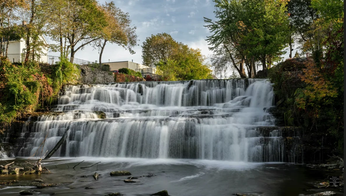Multi-tiered waterfall cascading through forested landscape with smooth water flow effect.