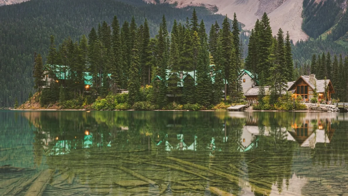 Lakeside cabins nestled among dense evergreen forest with mirror-like water reflection.