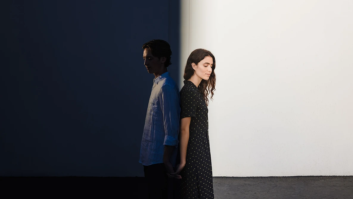 Two people standing against a minimalist backdrop with dramatic blue and white wall sections.