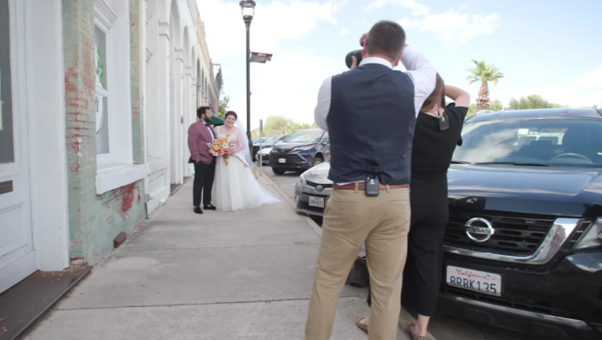 Wedding photographer capturing a bride and groom on a residential street lined with parked cars.