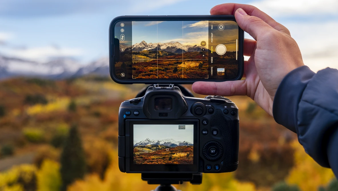 Smartphone and DSLR camera displaying the same mountain landscape scene during golden hour.