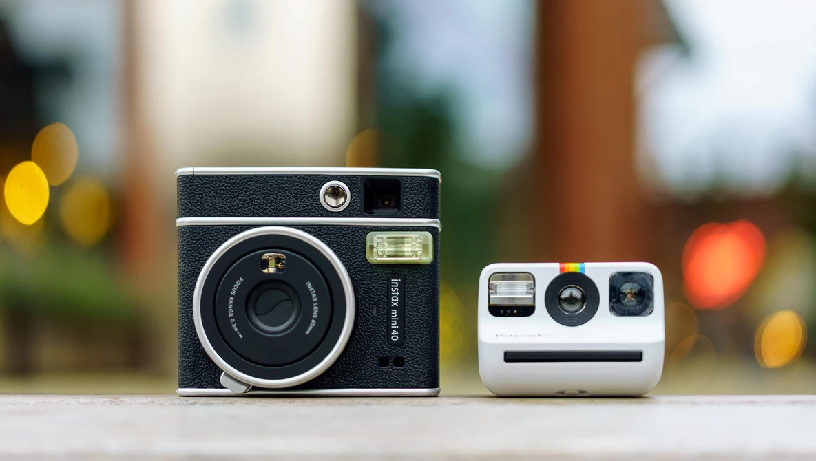 Vintage rangefinder camera next to a modern instant camera on a surface with blurred background lights.