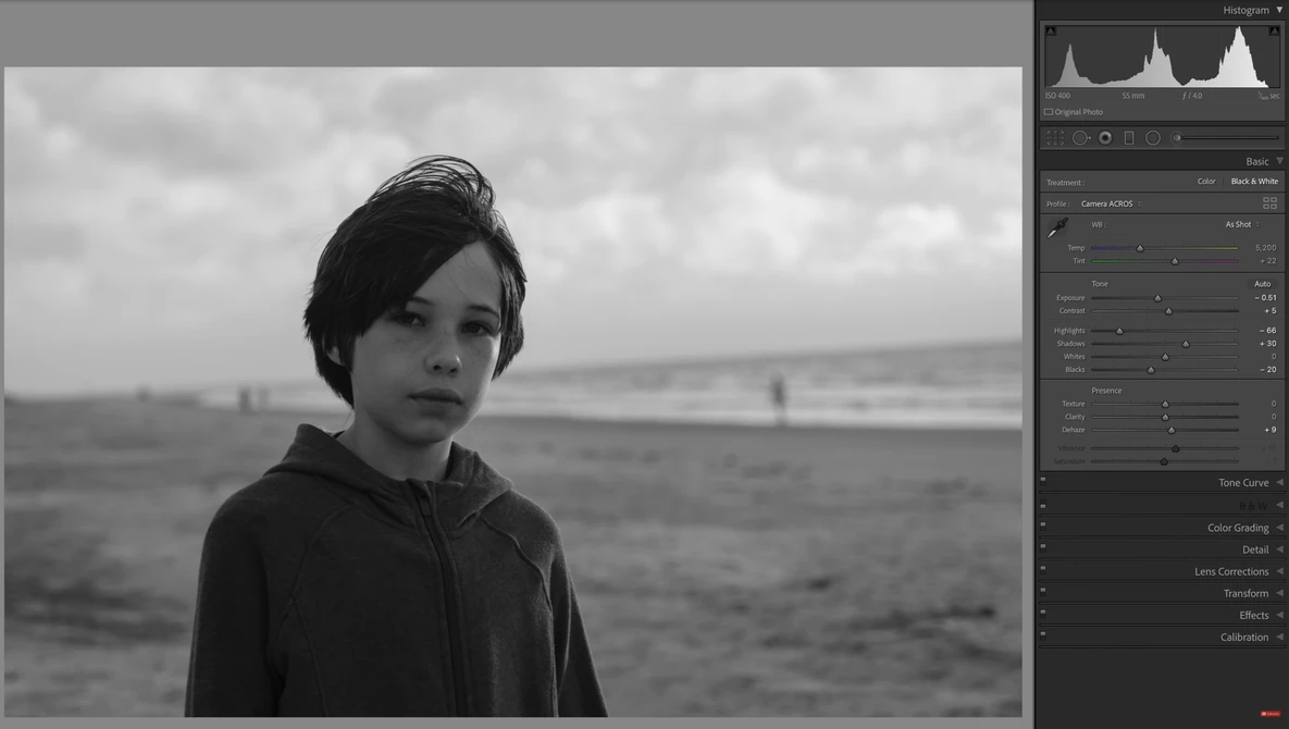 Young person in dark hoodie gazing toward horizon over calm water in black and white.