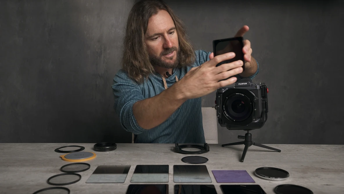 Photographer reviewing images on a smartphone while testing camera filters and gels at a workbench.