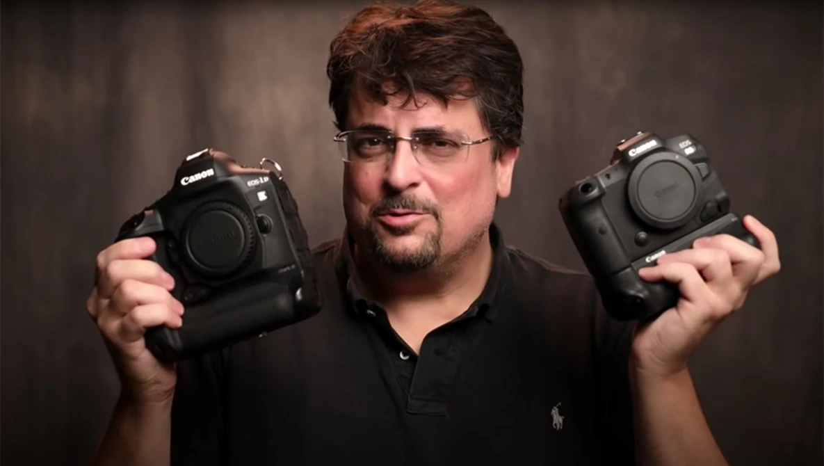 Photographer holding two professional DSLR camera bodies side by side for comparison.