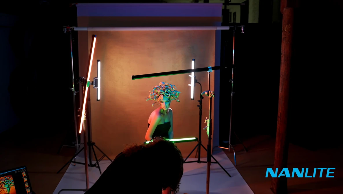 Studio portrait setup with subject in colorful clothing against warm-toned backdrop, illuminated by multiple neon light strips on stands.