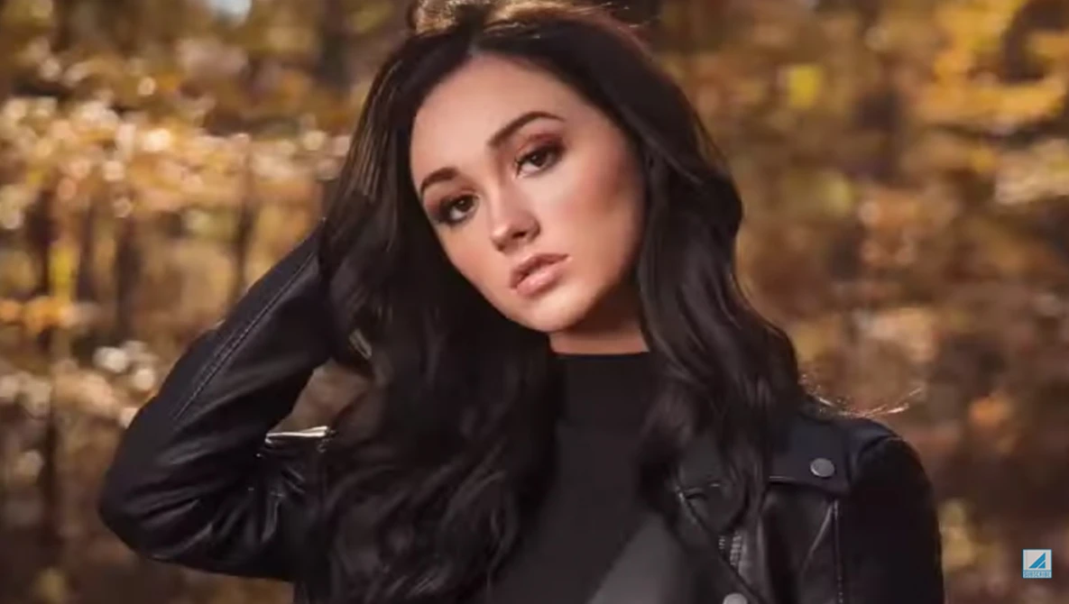 Woman with long dark hair wearing a black leather jacket against a golden bokeh background.