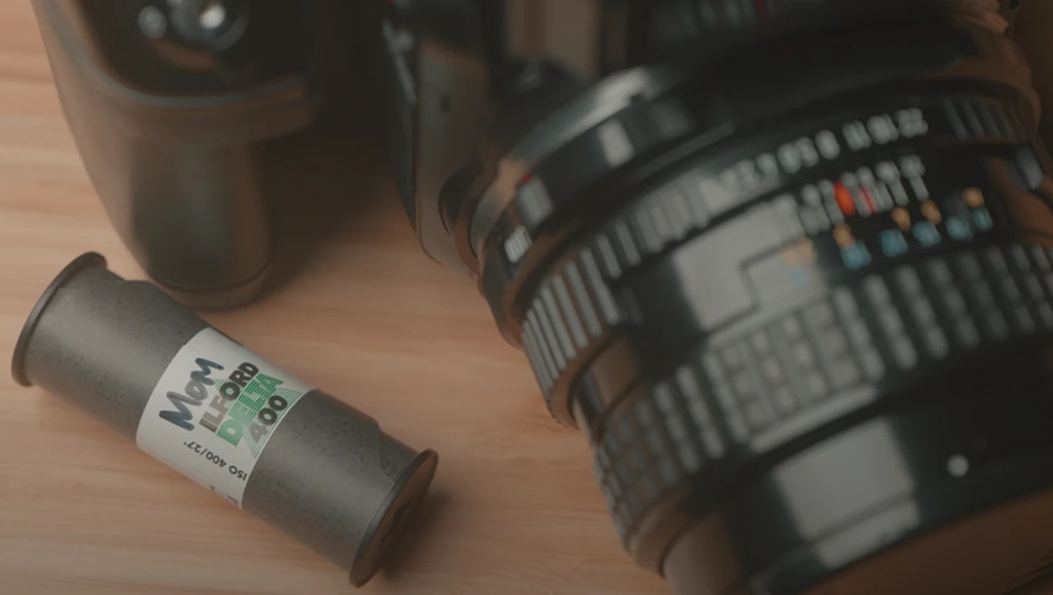 Film canister and camera lenses arranged on wooden surface.