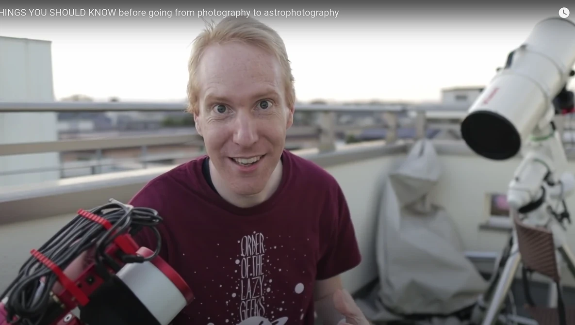 Person on a rooftop holding a camera and telescope, smiling at the camera.