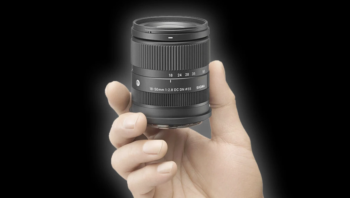 Hand holding a compact telephoto zoom lens with visible focal length markings and aperture information.