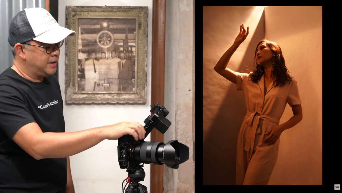 Photographer operating a mirrorless camera on tripod while model poses in warm studio lighting.