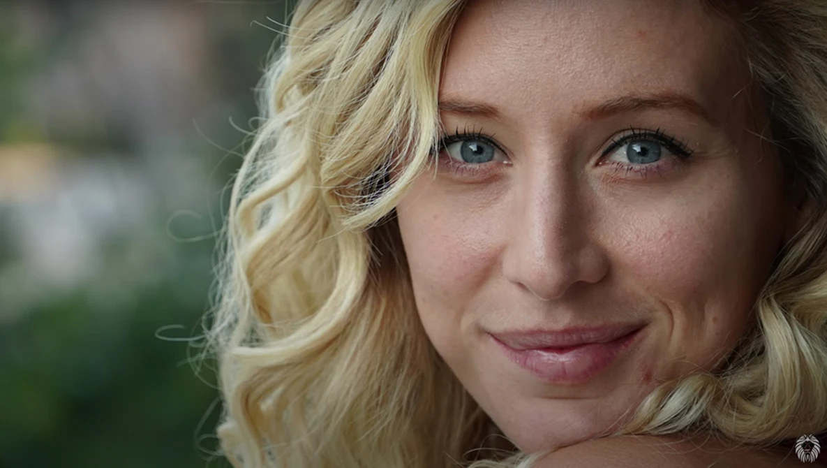 Blonde woman with wavy hair smiling at camera in natural outdoor light.
