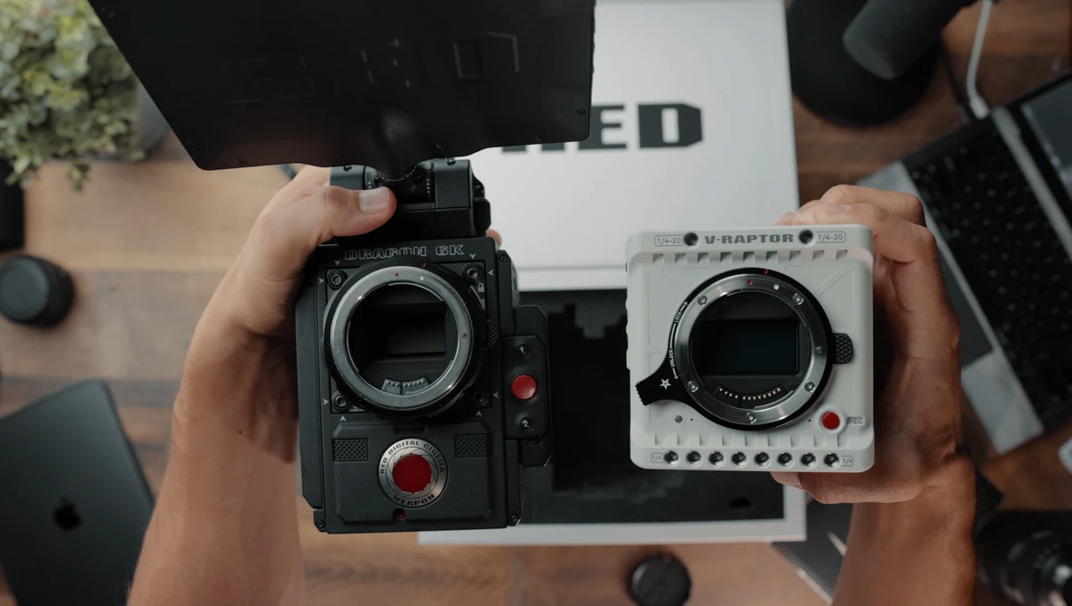 Two cinema cameras held side-by-side for comparison, one black and one white, both displaying their lens mounts and control interfaces.