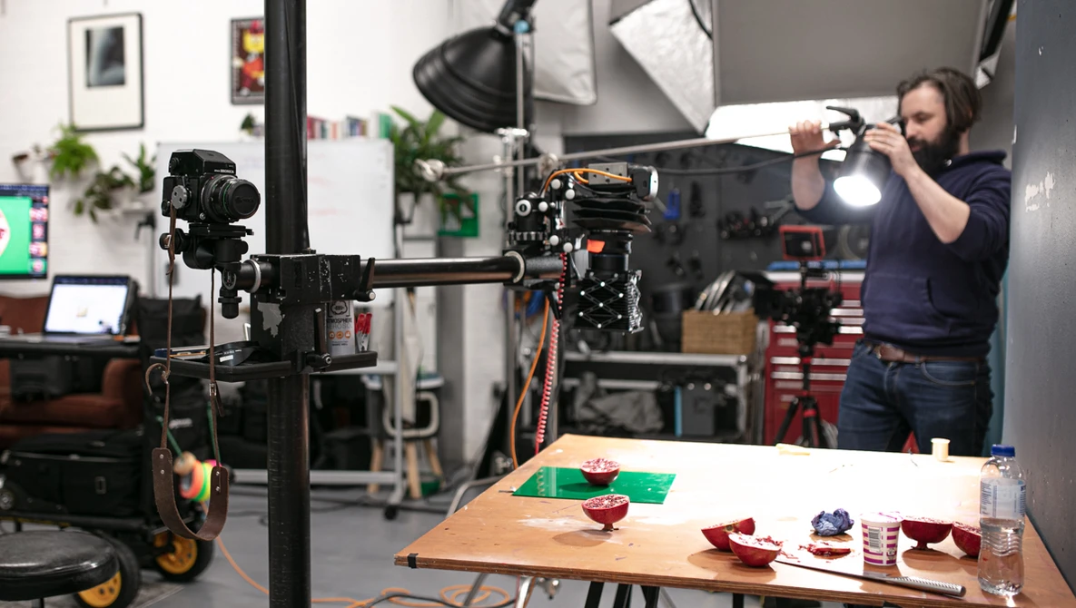 Cinematographer operating a camera on a jib arm in a studio with food photography setup below.