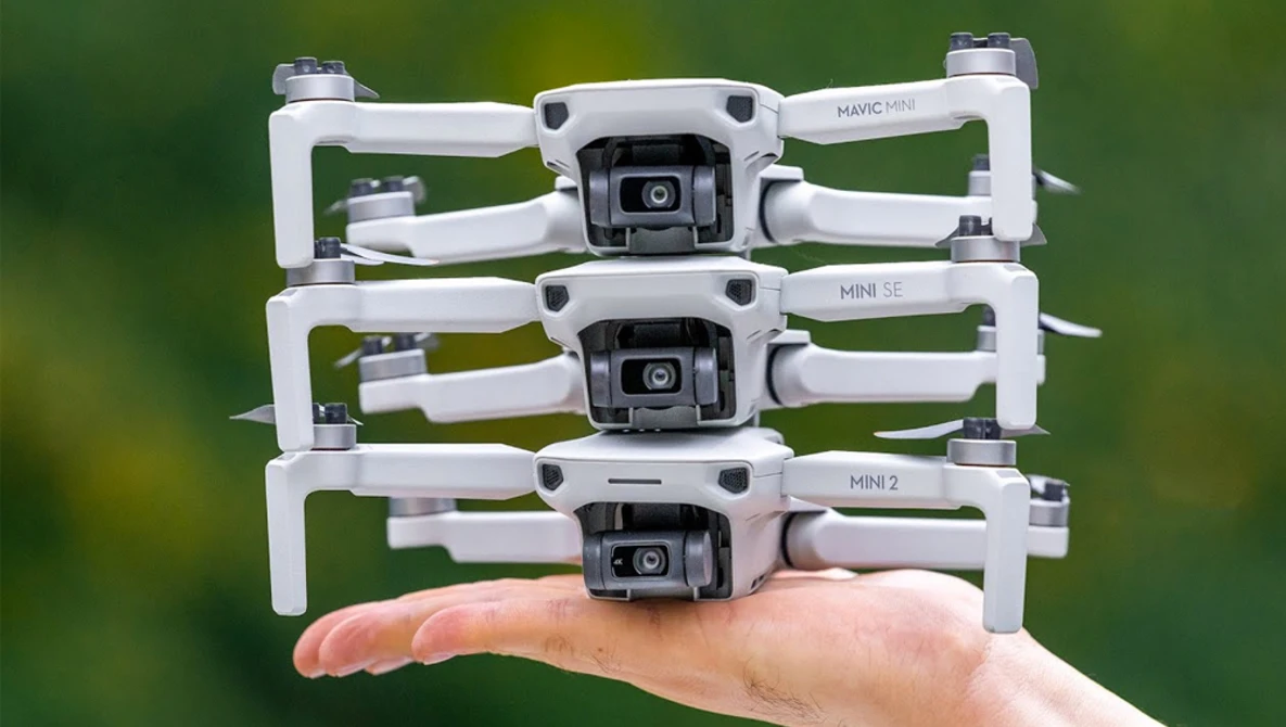 Three stacked compact drones displayed in a hand against a blurred green background.