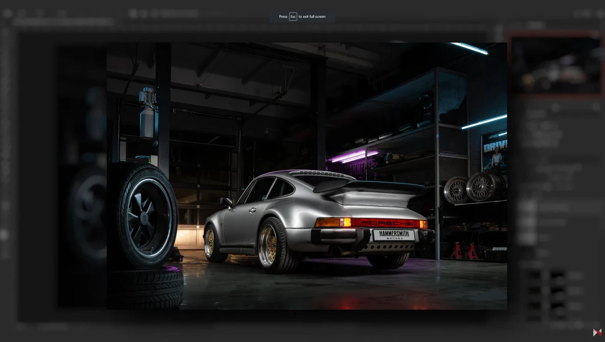 Silver Porsche 911 in a garage workshop with neon lighting and a large wheel display on the left wall.